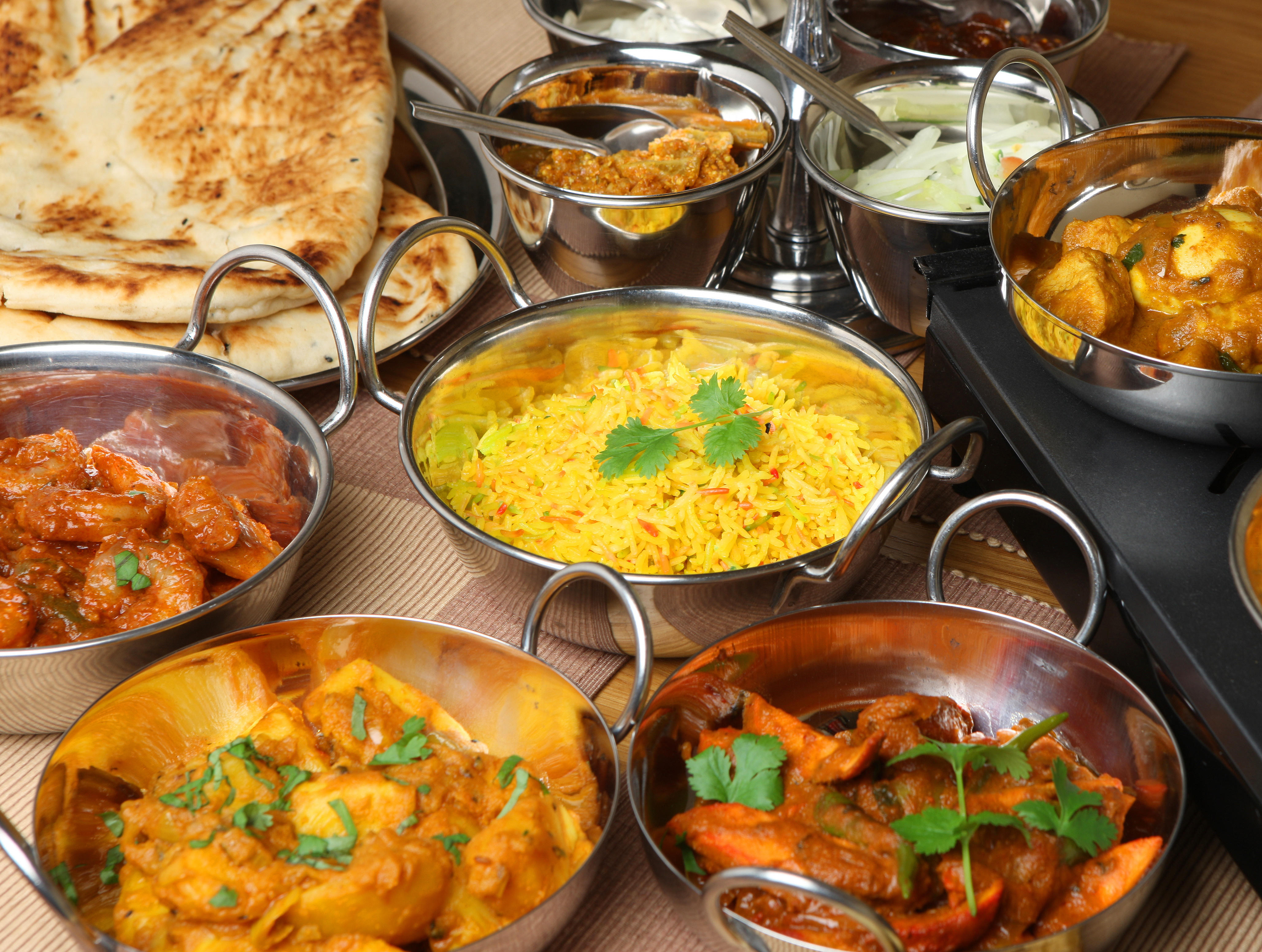 A spread of Indian curries, naan, and rice served in steel bowls