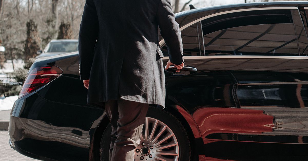 Professional chauffeur beside a black premium car