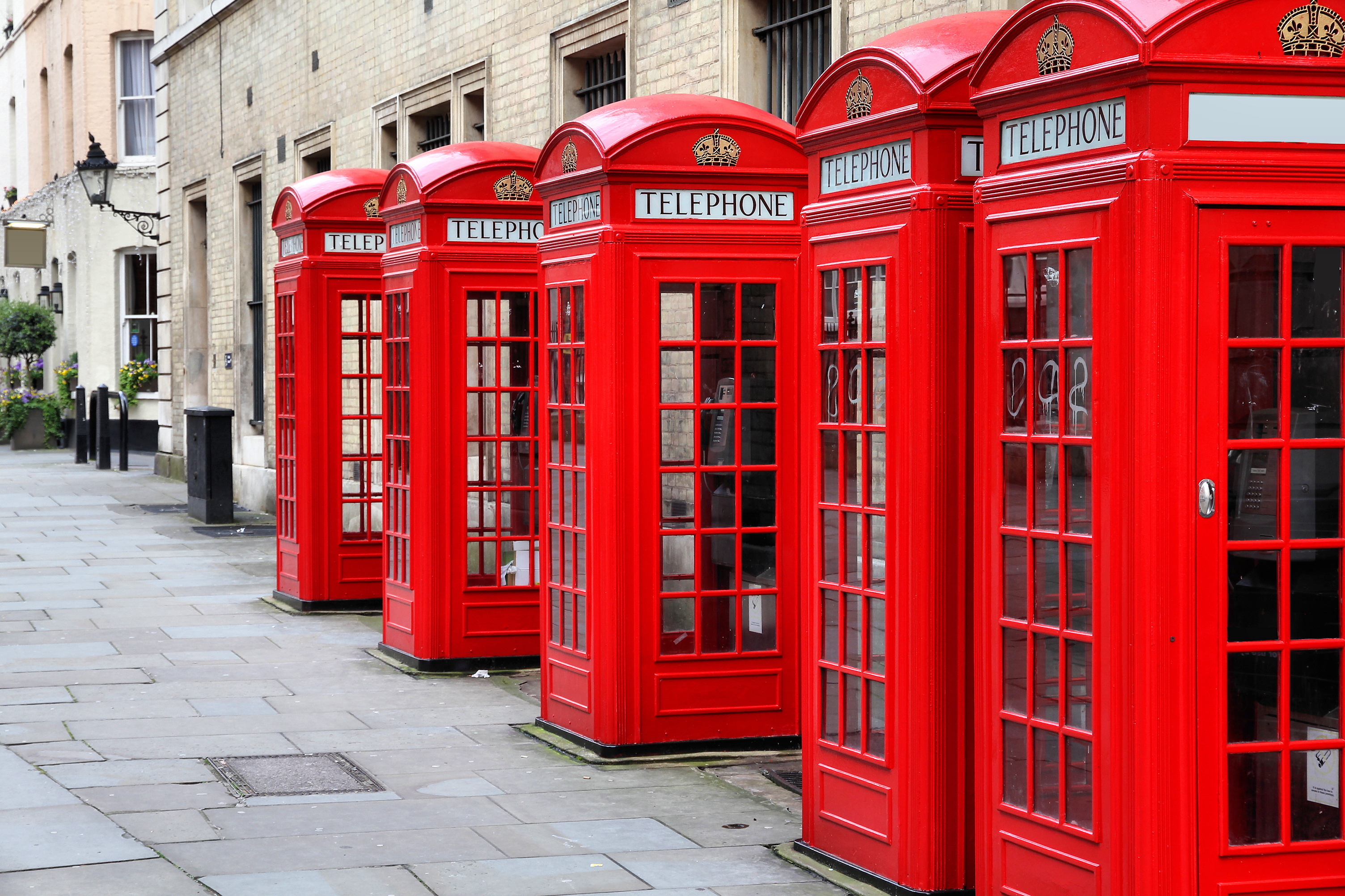A row of red London telephone boxes along a city sidewalk